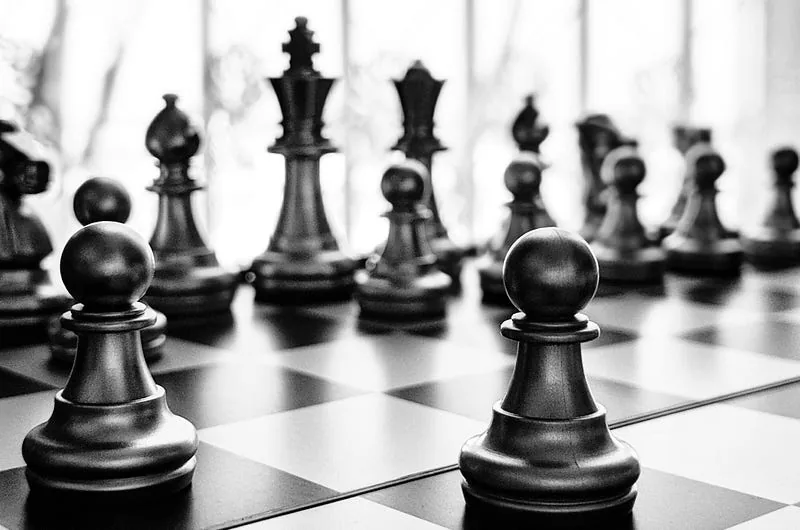 Black-and-white chess board with two pawns facing rows of opposing pieces in soft focus