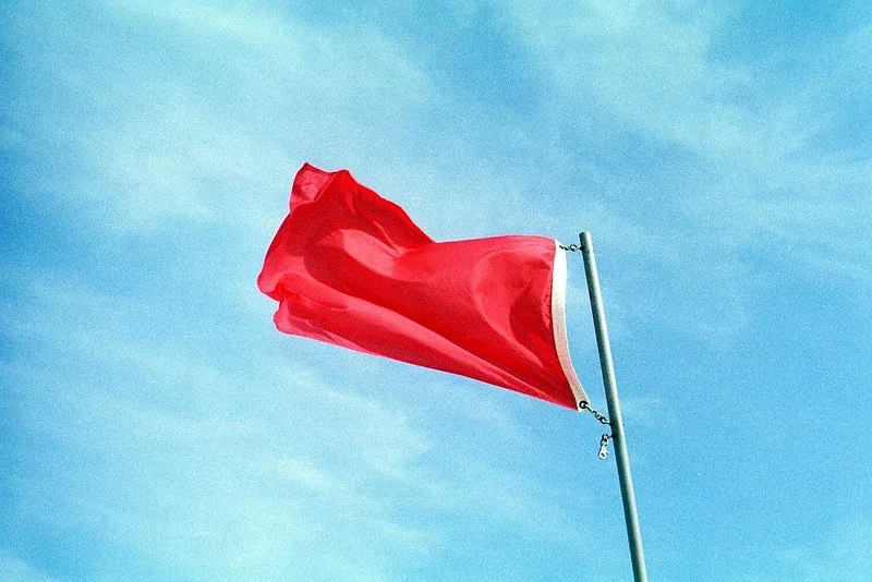 A single red flag flapping in the wind on a pole against a clear blue sky
